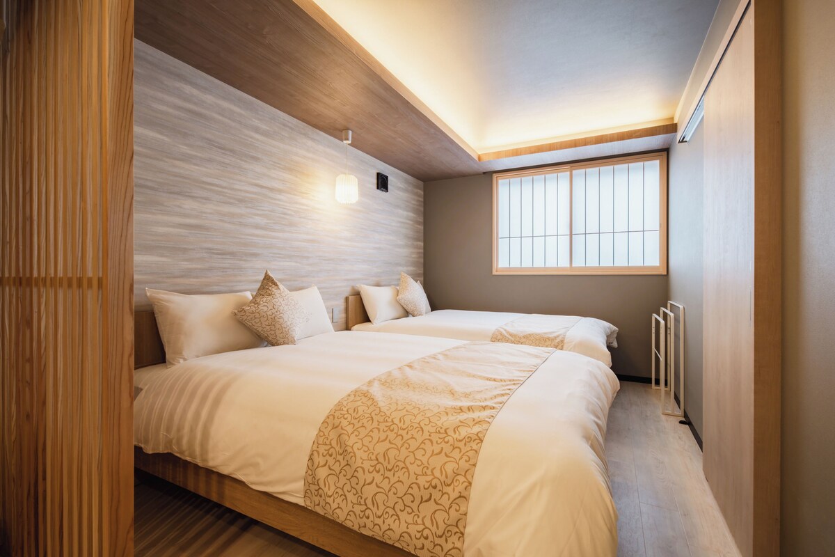 A modern bedroom with a large bed, a wooden headboard, a window with blinds, and a built-in heater.