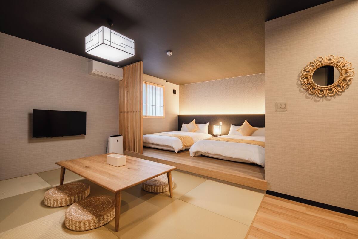 Una habitación de hotel moderna con una mesa de madera, dos camas, un televisor de pantalla plana y un espejo decorativo.