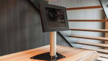 A modern, minimalist reception desk with a sleek, metallic frame and a black screen, positioned on a wooden counter with a staircase in the background.