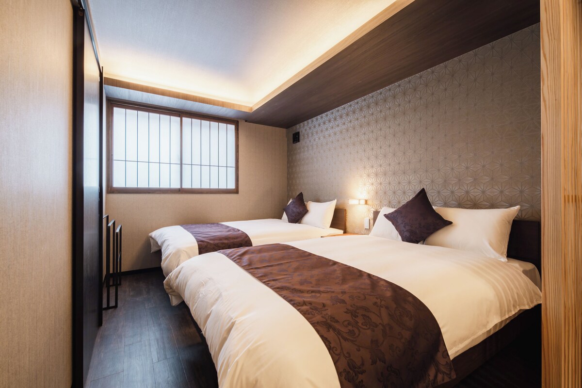 A hotel room with two beds, a large window, and a geometric patterned wall.
