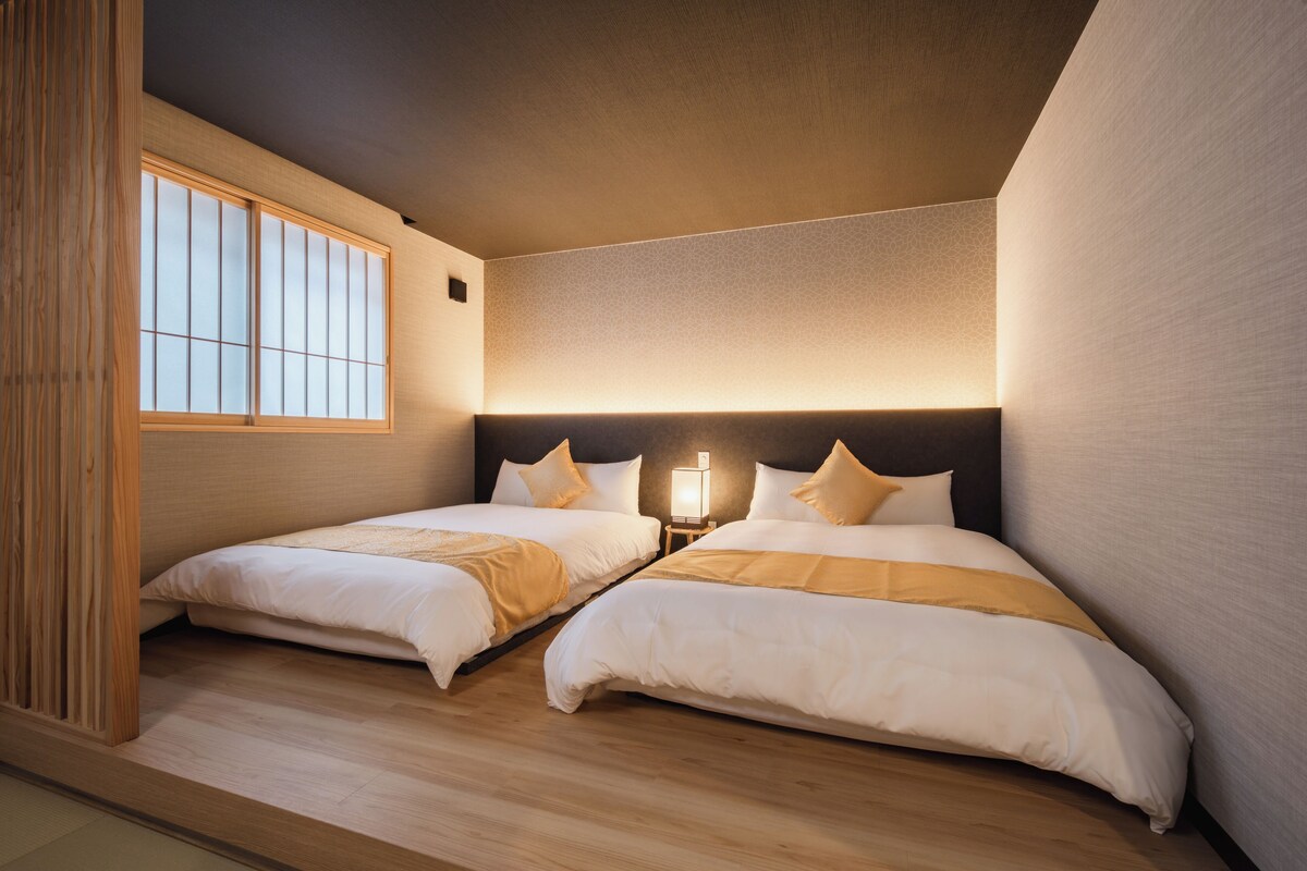 A hotel room with two beds, a window, and a nightstand with a lamp.