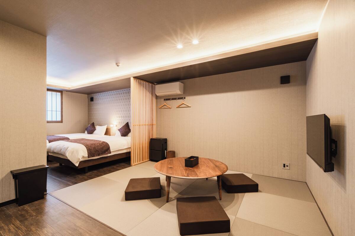 Una habitación de hotel moderna con una cama, una mesa redonda de madera, esteras de tatami, un televisor y un aire acondicionado instalado en la pared.