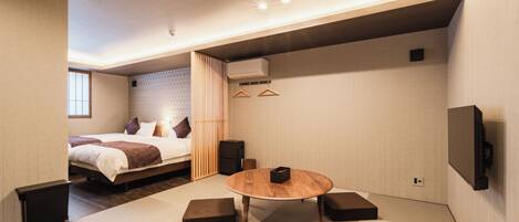 Une chambre d’hôtel moderne équipée d’un lit, d’une table ronde en bois, de tatamis, d’un téléviseur et d’un climatiseur fixé au mur.