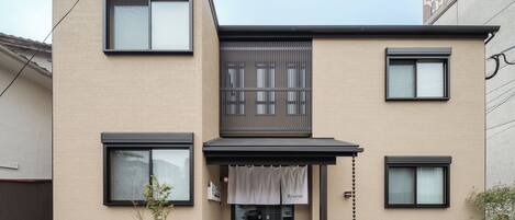 A modern two-story building with a beige facade, black-framed windows, and a covered entrance.