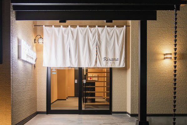 Ingresso di un hotel con uno striscione bianco che mostra il nome "Risana" e un cartello che indica area riservata ai non fumatori.