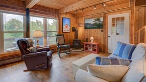 L’intérieur chaleureux d’un chalet avec une cheminée, des fauteuils en cuir, un canapé et de grandes fenêtres donnant sur le paysage extérieur.