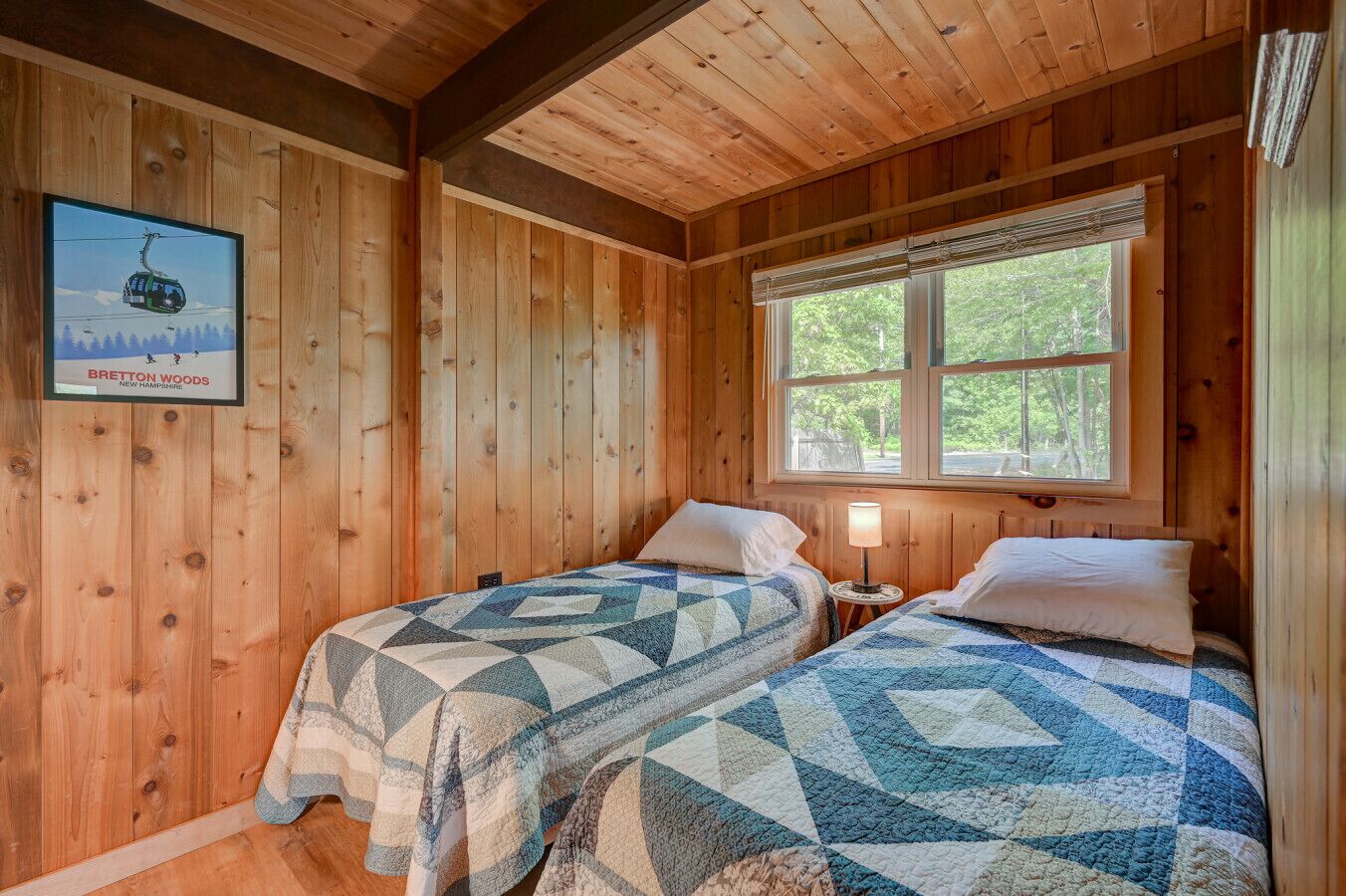 A cabin with two beds, a window with a view of trees, and a poster of a ski lift.