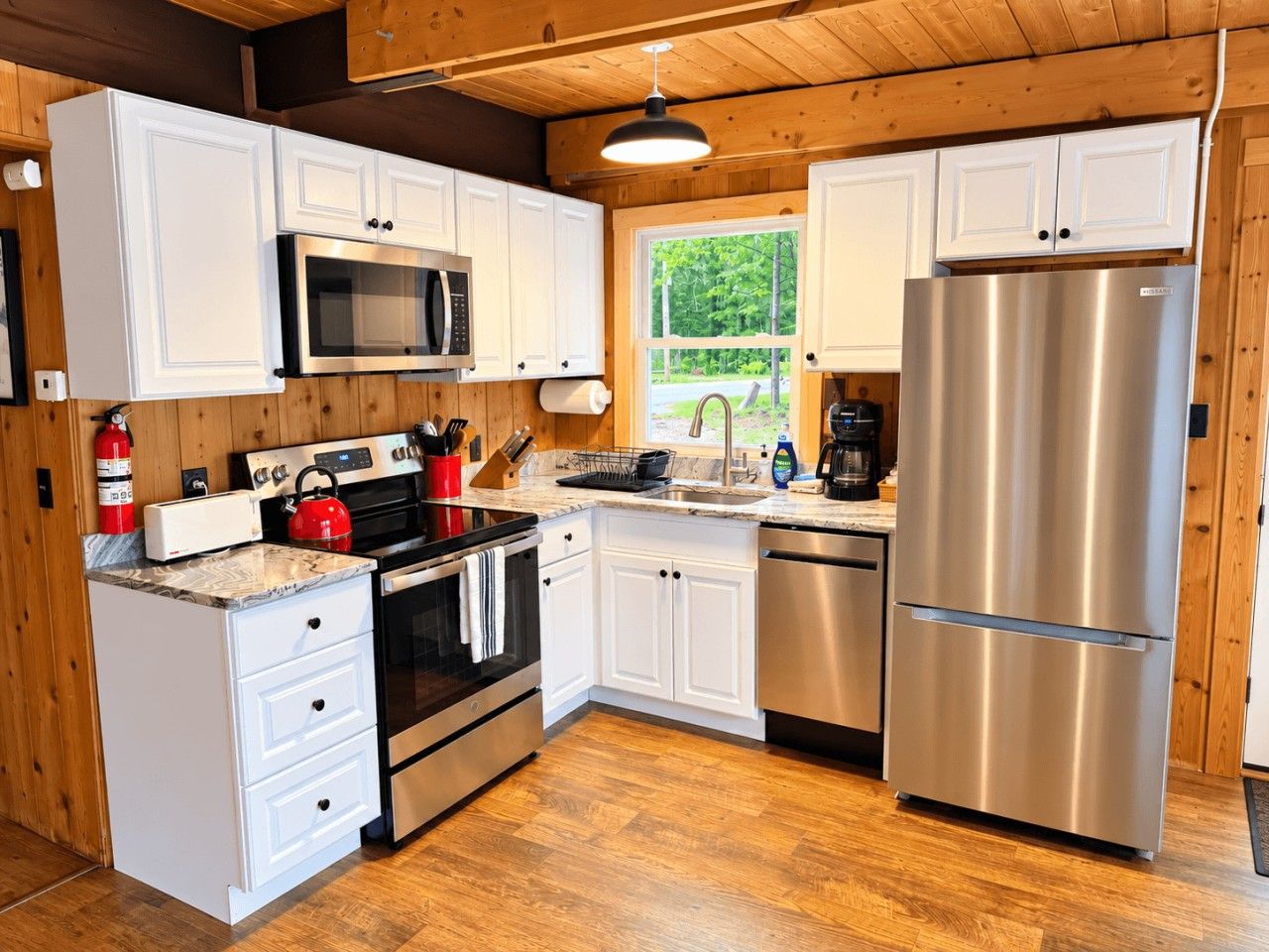 A compact kitchen with white cabinetry, stainless steel appliances, and a wooden floor.