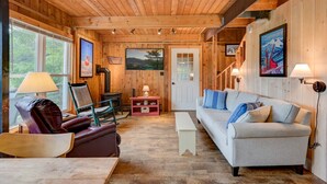 L’intérieur chaleureux d’un chalet avec un plafond en bois, une cheminée, un canapé, un fauteuil à bascule et une table à manger.