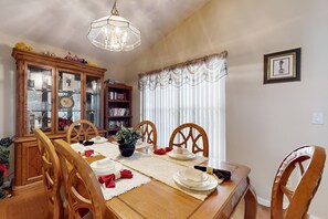 A dining room with a wooden table, chairs, a chandelier, a cabinet with glass doors, and a bookshelf. - 15 Min to Disney | Spacious 4BR Home w/ Pool (Kissimmee)