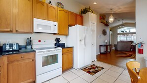 A kitchen with wooden cabinets, a white stove, a microwave, and a refrigerator. There is a dining area with a table and chairs. - 15 Min to Disney | Spacious 4BR Home w/ Pool (Kissimmee)