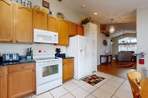 A kitchen with wooden cabinets, a microwave, a stove, and a refrigerator. There is a dining area with a table and chairs. - 15 Min to Disney | Spacious 4BR Home w/ Pool (Kissimmee)