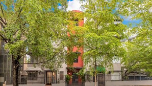 Un edificio con fachada roja, rodeado de árboles y una entrada protegida por una reja.