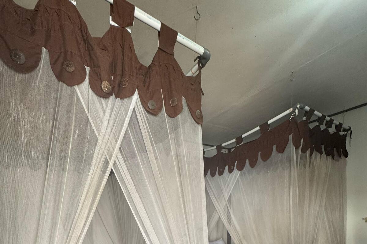 Deux lits en bois, dotés de draps blancs et de têtes de lit marron, et protégés par un moustiquaire.