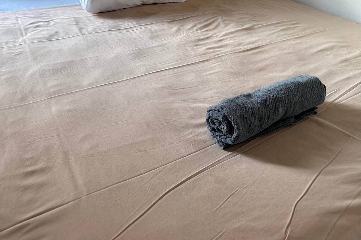Un lit bien fait, avec une tête de lit en bois, une serviette enroulée et deux oreillers blancs.