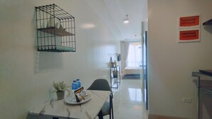 A hotel room with a dining area, a bed, a small table with a plant and water bottles, and a wall-mounted birdcage.