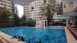 An indoor swimming pool with multiple lanes, surrounded by trees and a multi-story building with balconies.
