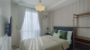 A bedroom with a bed, a bedside table with a lamp, a wall-mounted air conditioner, and a wooden shelf.