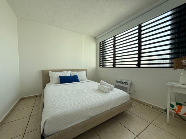 A single-bed room with a white bedspread, a blue pillow, and a white radiator.