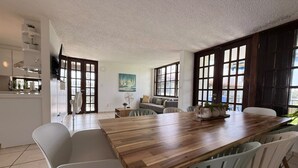 Un comedor con una mesa de madera, sillas blancas y vistas a la cocina y la sala de estar.