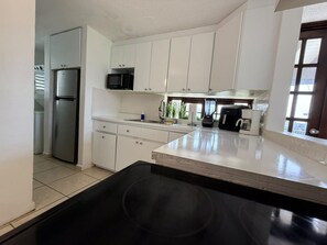 A kitchen with white cabinets, a stainless steel refrigerator, a microwave, and a coffee maker. - Playas Del Yunque | Beach Apt W/Pool In Rio Geande (Río Grande)