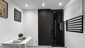 Un comedor moderno con una mesa blanca para cuatro, una puerta oscura y una ventana con persianas.