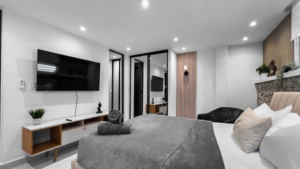 Un dormitorio moderno con una cama grande, un televisor montado en la pared, una mesita de noche y un armario.