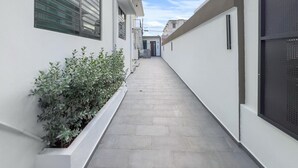 Un callejón estrecho y limpio, con un edificio blanco a un lado y una valla de metal al otro.