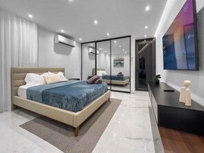 Ein modernes Schlafzimmer mit einem großen Bett, einem Schreibtisch und einem an der Wand befestigten Fernseher.