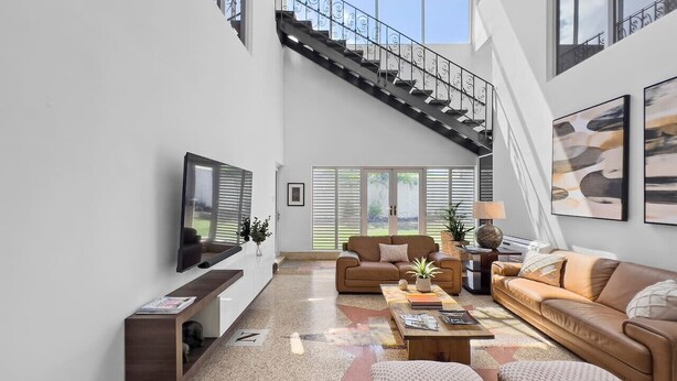 Un salon spacieux avec un haut plafond, un escalier et de grandes fenêtres.