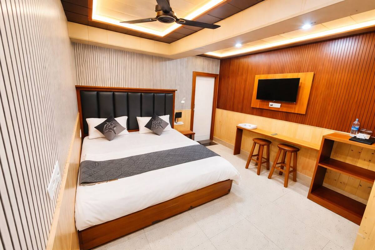 A modern hotel room with a large bed, a desk, a TV, and a ceiling fan.