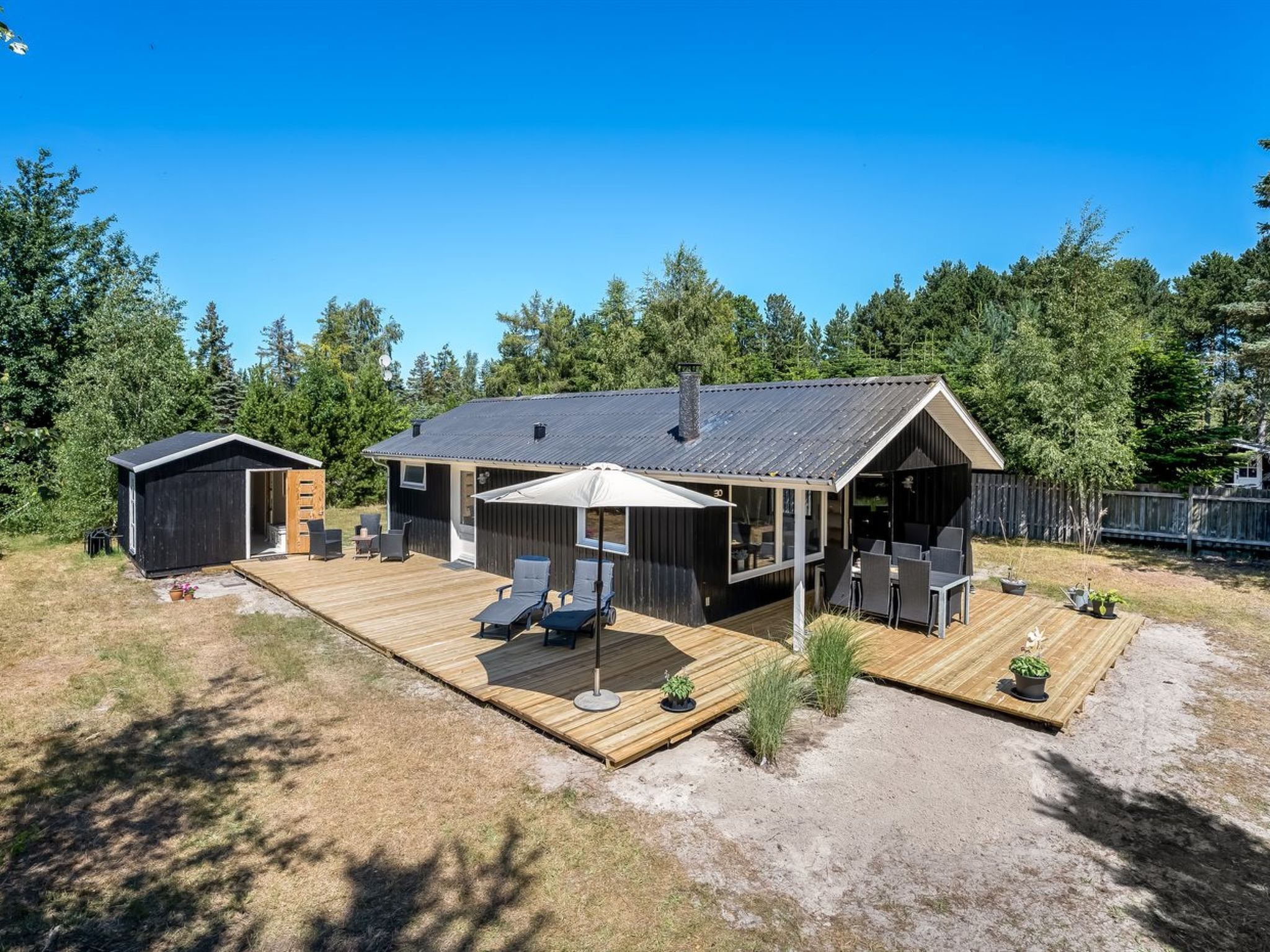 A modern cabin with a deck, outdoor seating, and a small shed.