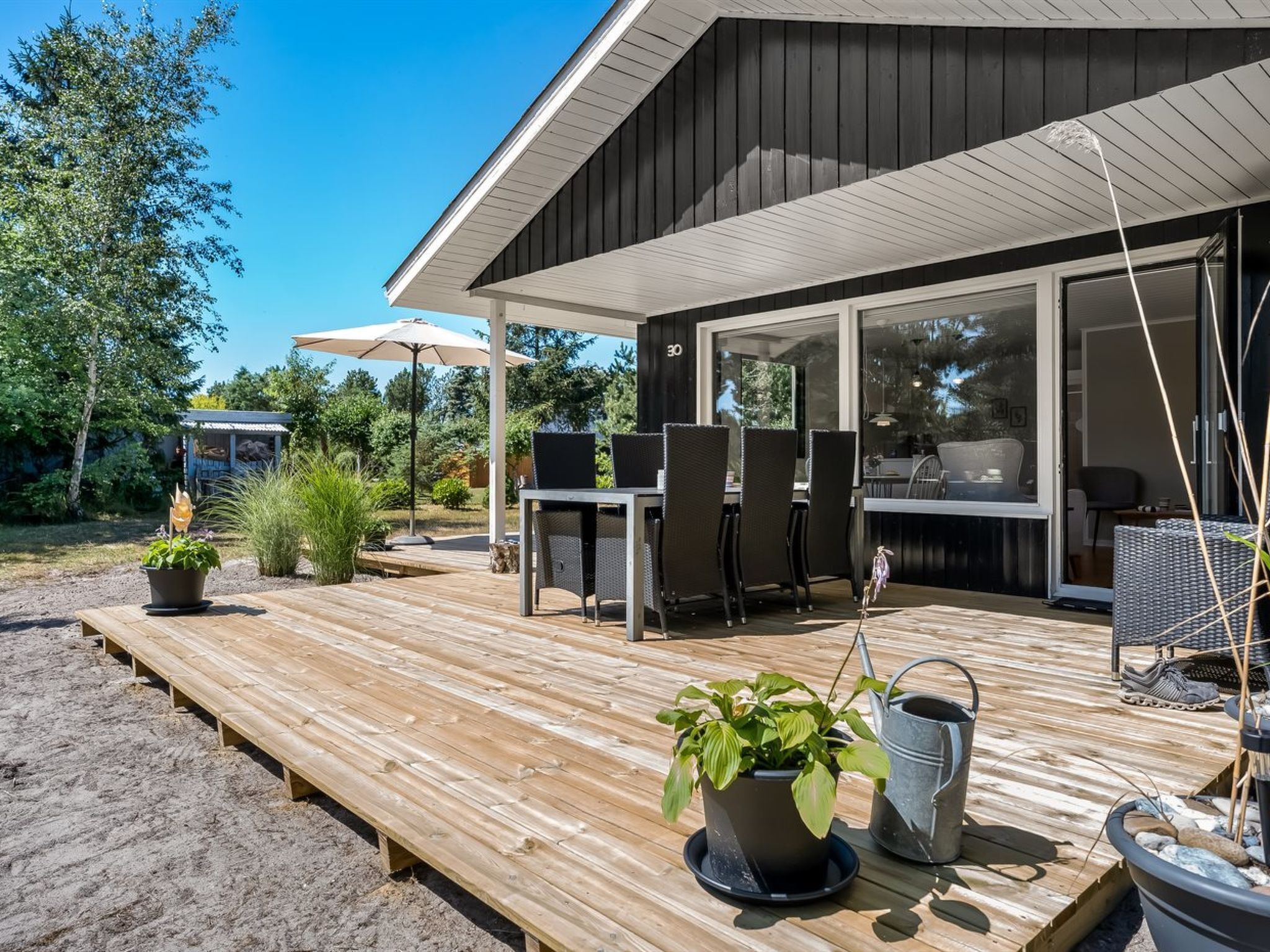 Una terraza de madera con mobiliario exterior, una pérgola y vistas al interior.