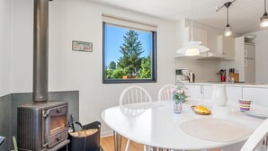 Eine moderne Küche mit Kaminofen, weißen Schränken und einem großen Fenster mit Blick auf Bäume.