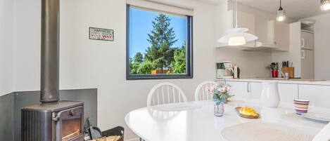 A modern kitchen with a wood-burning stove, white cabinetry, and a large window with a view of trees.