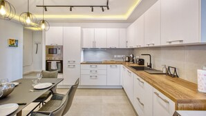 A modern kitchen with white cabinets, a wooden countertop, and a dining area with a table and chairs.