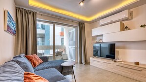 A modern living room with a grey sofa, a flat-screen TV, and a balcony with a view of the city.