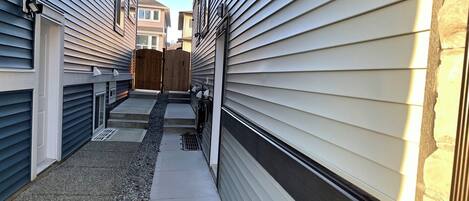 A narrow residential alleyway with houses on either side, a wooden fence, and a concrete pathway.