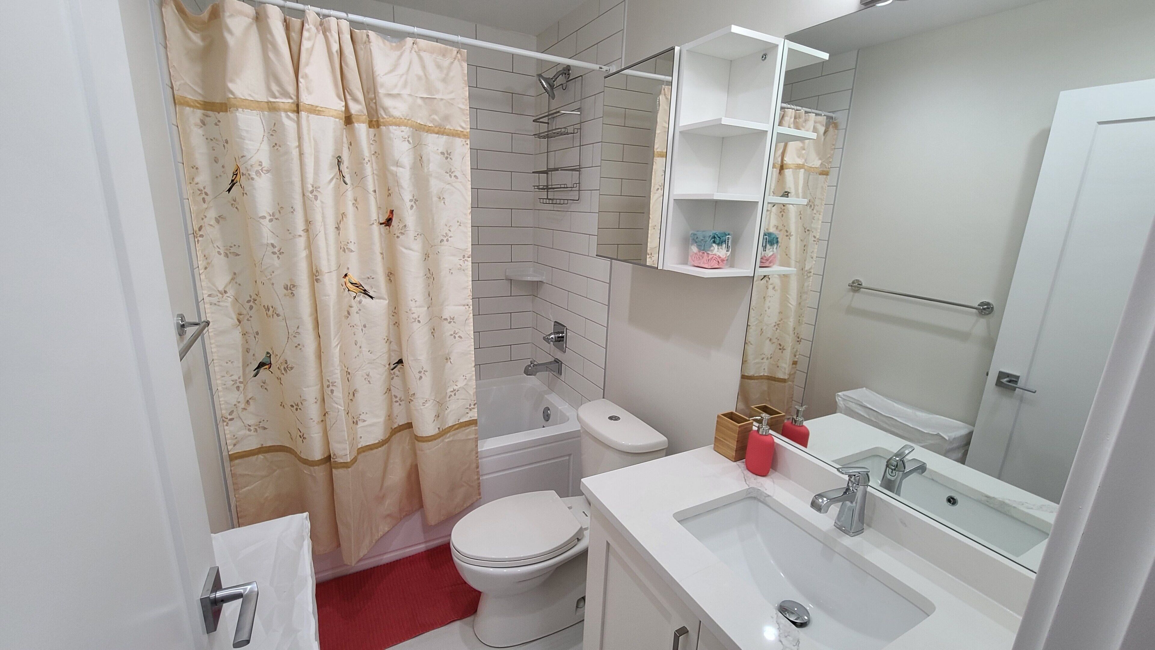 A bathroom with a shower curtain, toilet, sink, and shelves.