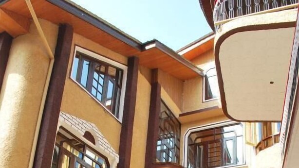 A multi-story building with balconies, a car, and a motorcycle parked in front. - Hotel Gulistan (Srinagar)