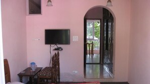 A bedroom with a bed, a television, a desk, and a chair. There is a large window with an arched doorway leading outside. - Hotel Gulistan (Srinagar)