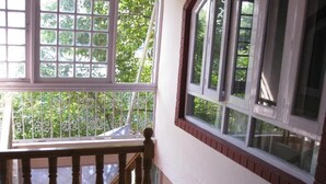 A wooden staircase with a railing leading to a balcony with large windows overlooking greenery. - Hotel Gulistan (Srinagar)