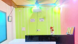 A reception area with a reception desk, a ceiling fan, a wall-mounted air conditioner, and a sign indicating check-out time. - Shri Raghav Kunj 200 Mtr from RAM Temple (Faizabad)