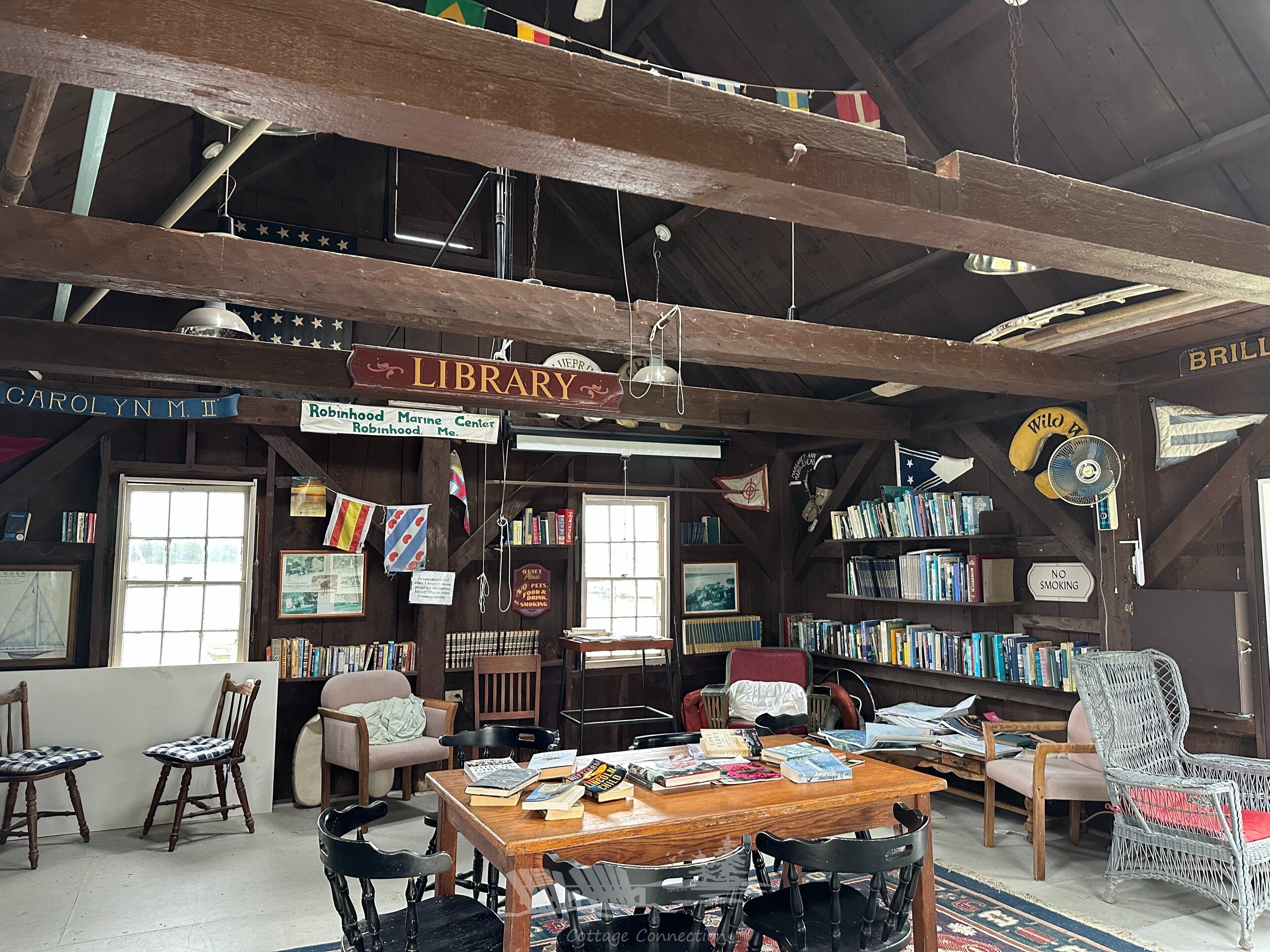 Een rustieke bibliotheek met houten balken, een bord met daarop 'Library' en boekenplanken vol boeken.