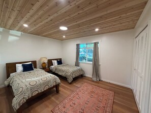 Ein Schlafzimmer mit zwei Betten, Holzboden, einem Fenster mit Vorhängen und einer Holzziel.
