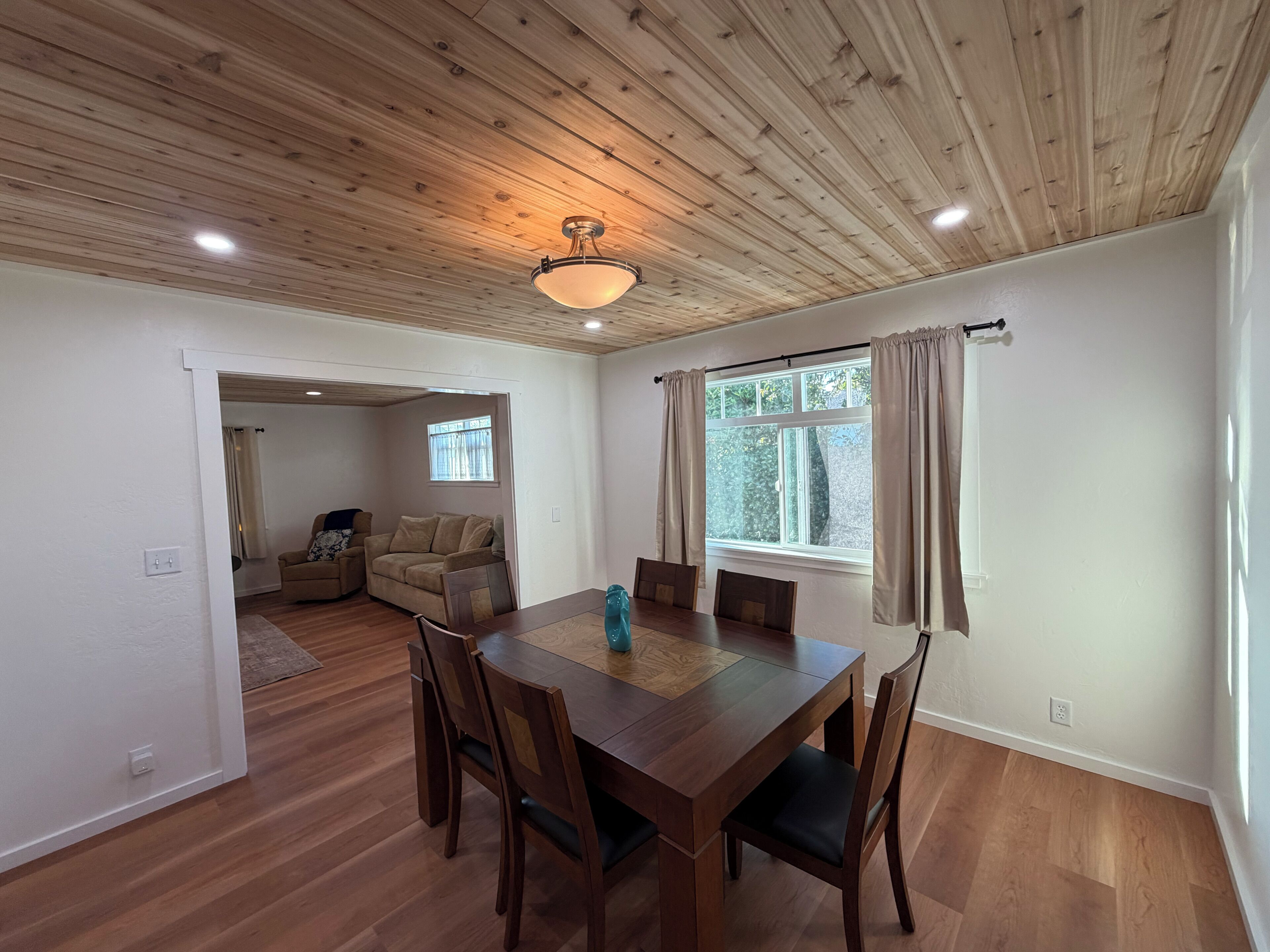 Un comedor con una mesa y sillas de madera, un techo con vigas de madera y una ventana con cortinas.