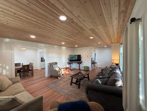A living room with a wooden ceiling, a TV, a sofa, a coffee table, and a dining area with a table and chairs.
