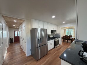 A modern kitchen with stainless steel appliances, wooden flooring, and a dining area with a table and chairs.