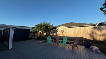Un patio trasero con terraza de madera, un árbol y sillas Adirondack de colores.