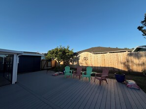 A backyard with a wooden deck, a tree, and colorful Adirondack chairs.